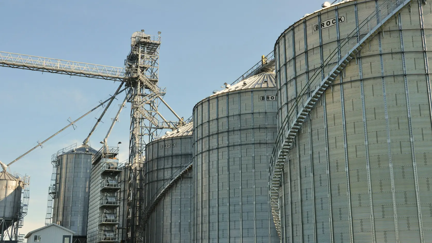 Moderne Futtermühle mit Stahlgetreidesilos und Fördersystemen unter klarem Himmel.